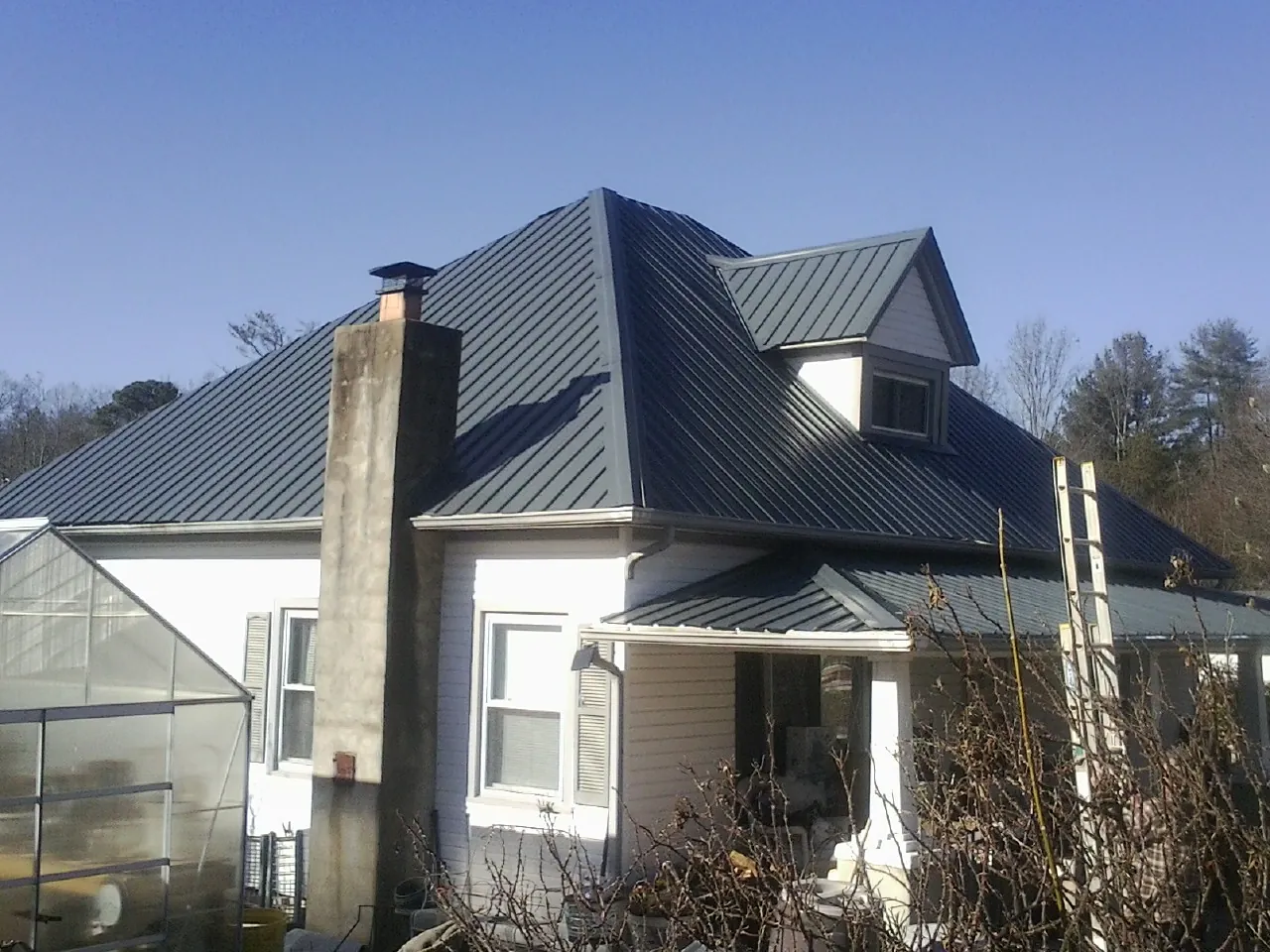 Dark blue standing seam metal roof on a white farmhouse with dormer — Slate & Tile Roof Repair by Roofing Brothers in Cobbtown