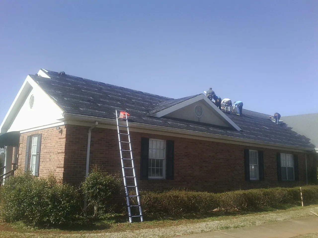 Crew tearing shingles off a brick ranch roof with a ladder set — Emergency Roof Repair work by our crew in Cobbtown