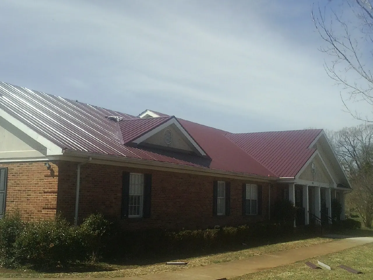 Red metal roof with gabled entries on a long brick building, from a Hail Damage Roof Repair job in Cobbtown