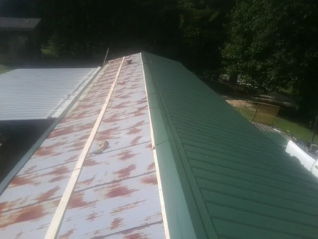 Old rusted panels beside newly installed green metal roofing — Wind Damage Roof Repair by Roofing Brothers in Cobbtown