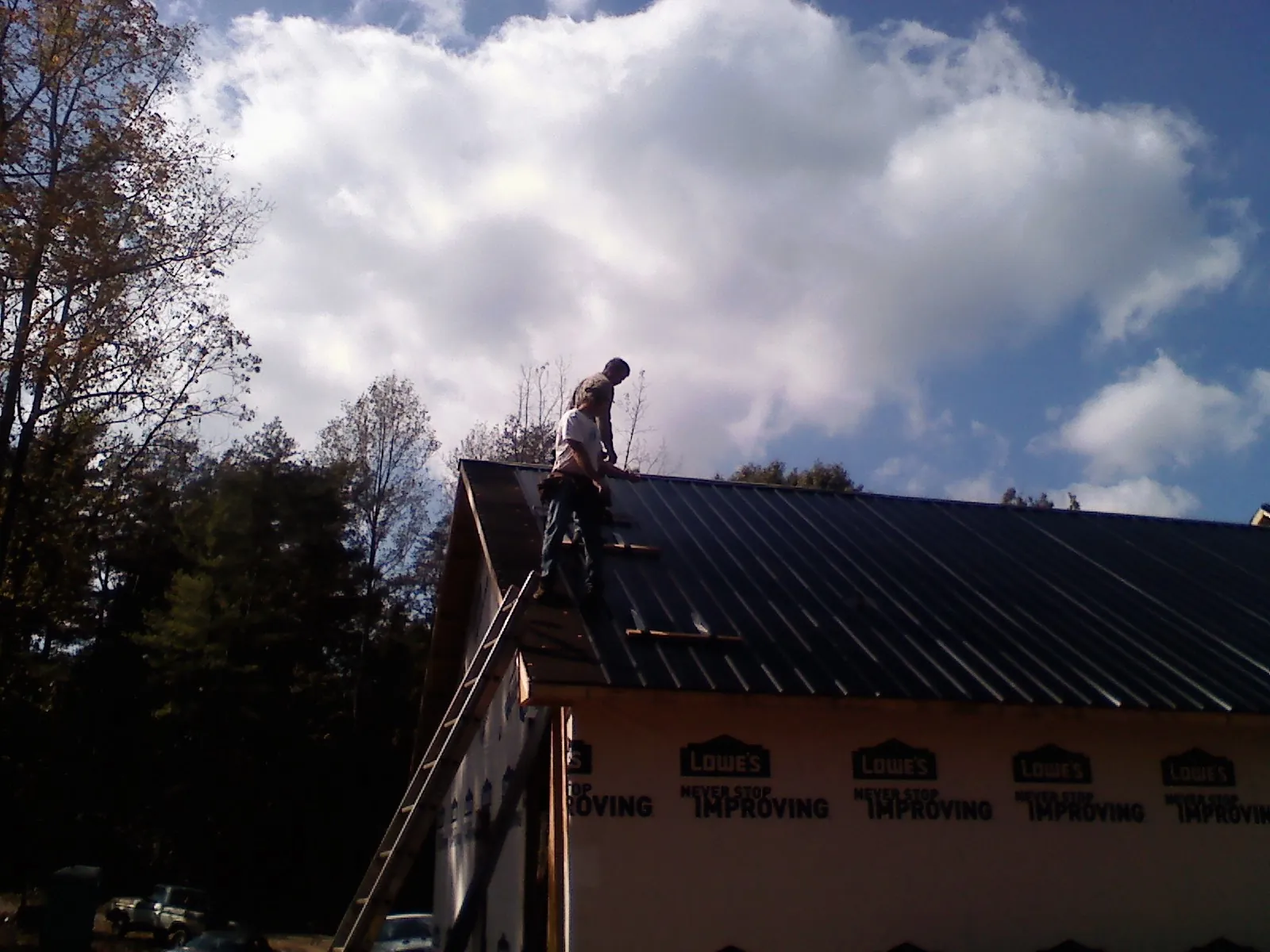 Roofer fastening dark metal panels high against a cloudy sky, from a Roof Inspection job in Cobbtown