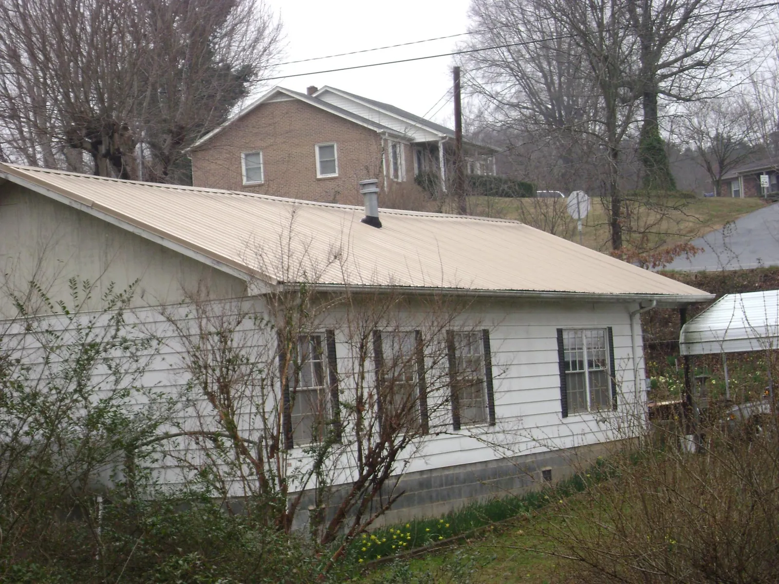 Tan metal roof on a white sided house set into a hillside — Commercial Roofing by Roofing Brothers in Cobbtown
